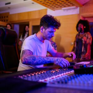 Audio music producer operating on a mixing console in a music studio.