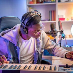 Black man artist recording music while playing electronic piano at home studio.